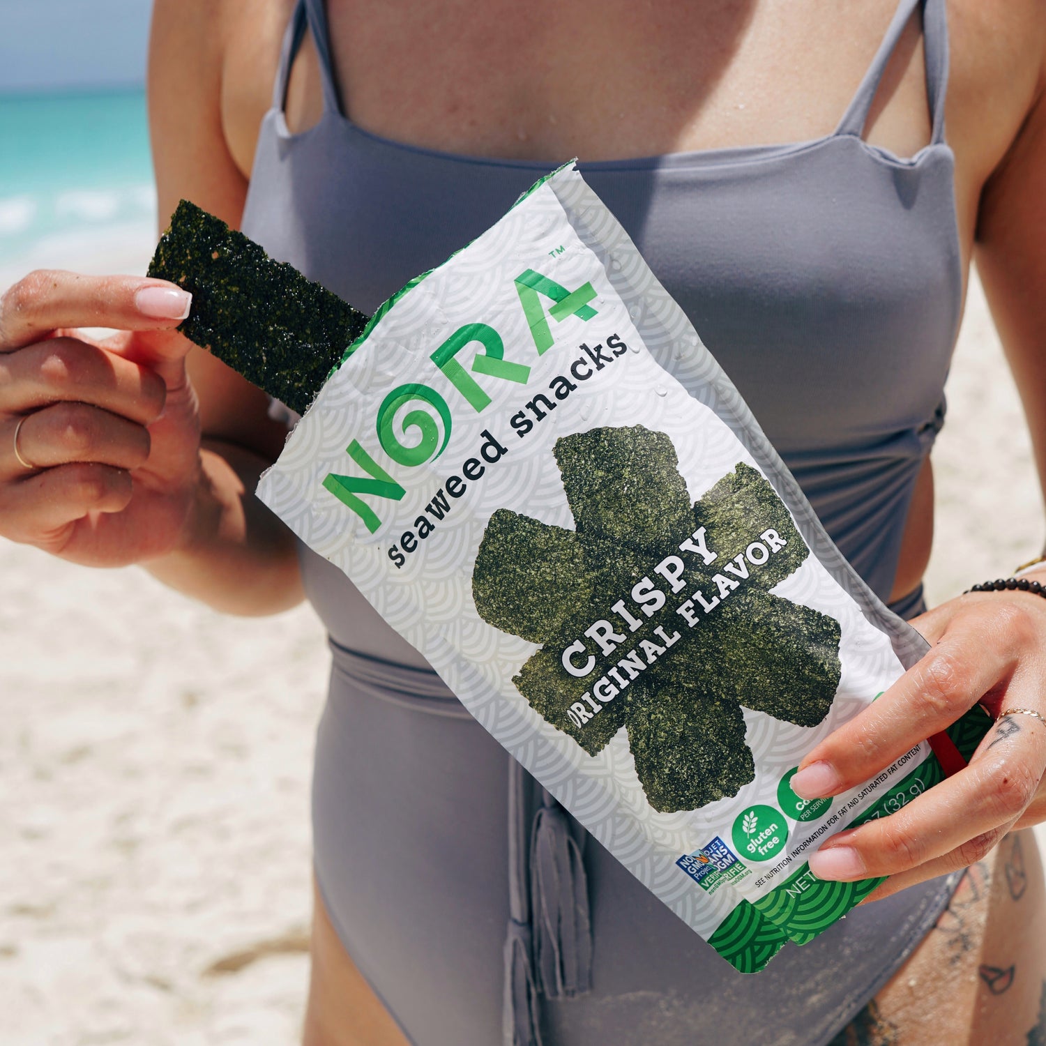 Young woman at a beach enjoying Nora Seaweed Snacks.