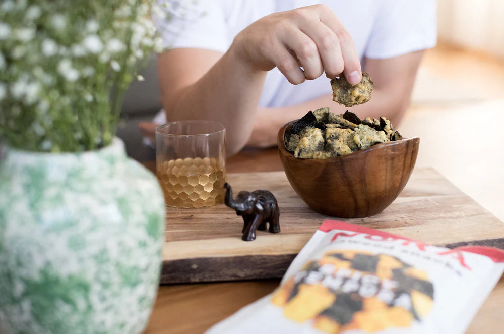 A bowl of Nora Seaweed Snacks placed on a table. A person sits in front enjoying the snacks.
